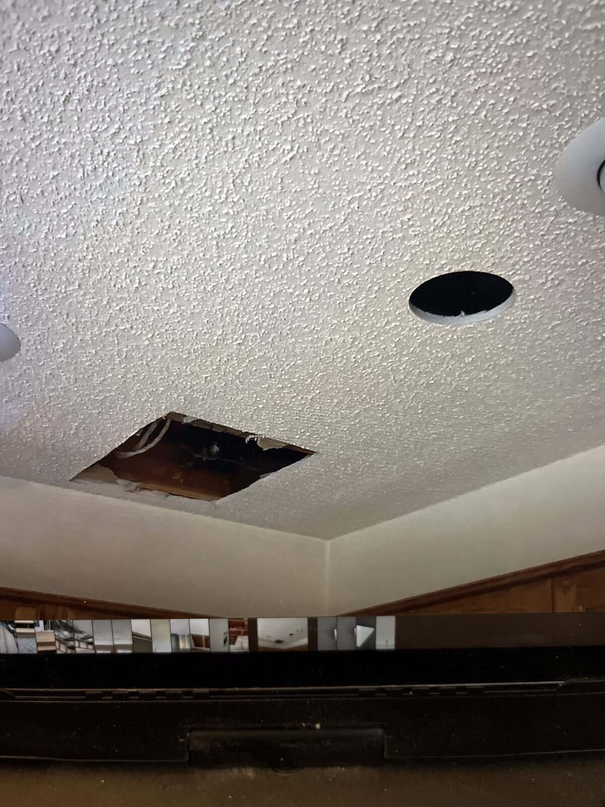 A damaged ceiling with a hole and an exposed area, likely in a residential or commercial property, with a smoke detector nearby.