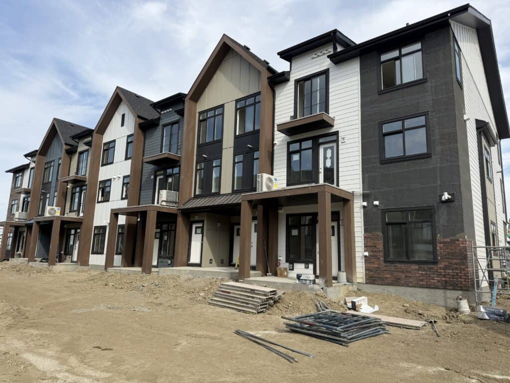 A residential building under construction with modern black, white, and brown exterior siding, large windows, and a small front porch in a developing.