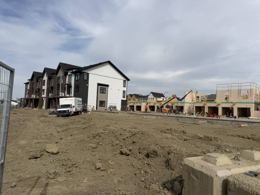 A construction site with newly built residential houses and ongoing framing work under a cloudy sky.