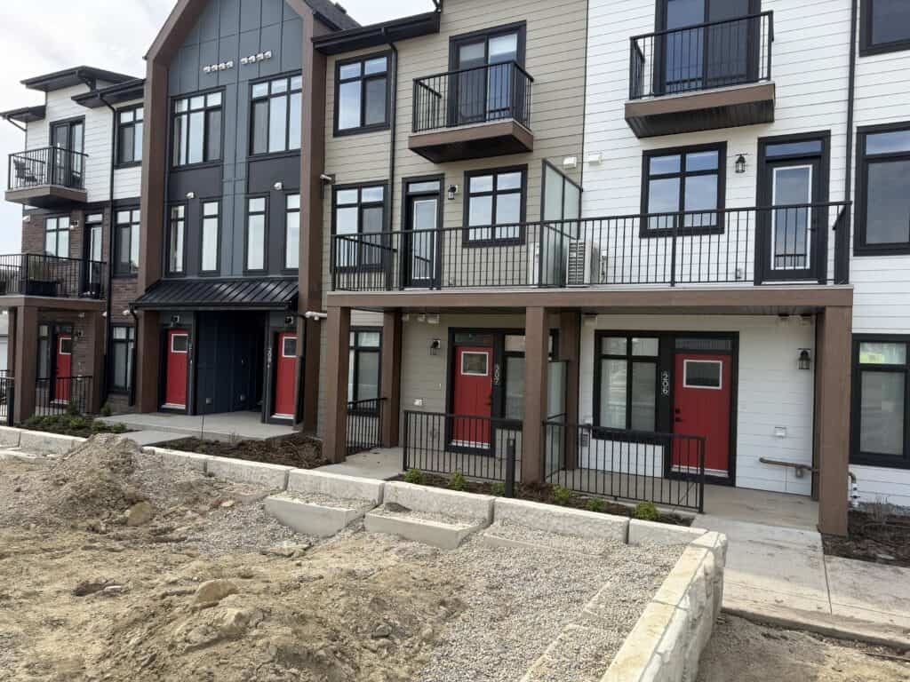 A modern multi-story residential building with colorful exterior walls, black balconies, and red front doors, under construction in an urban area.