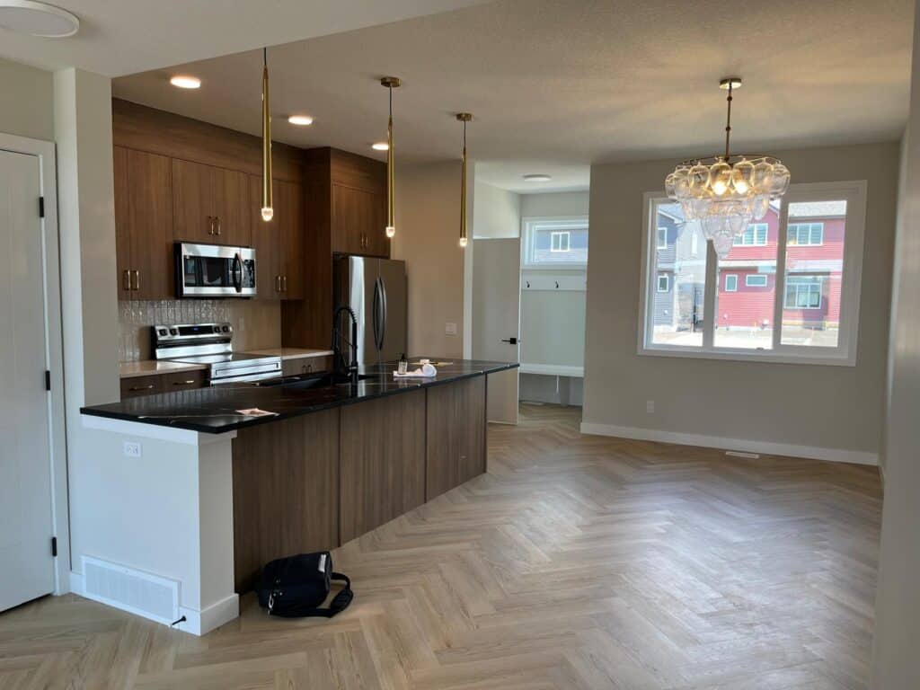 A modern open-concept kitchen and dining area with wooden cabinets, stainless steel appliances, large windows, and a stylish chandelier in a residenti.