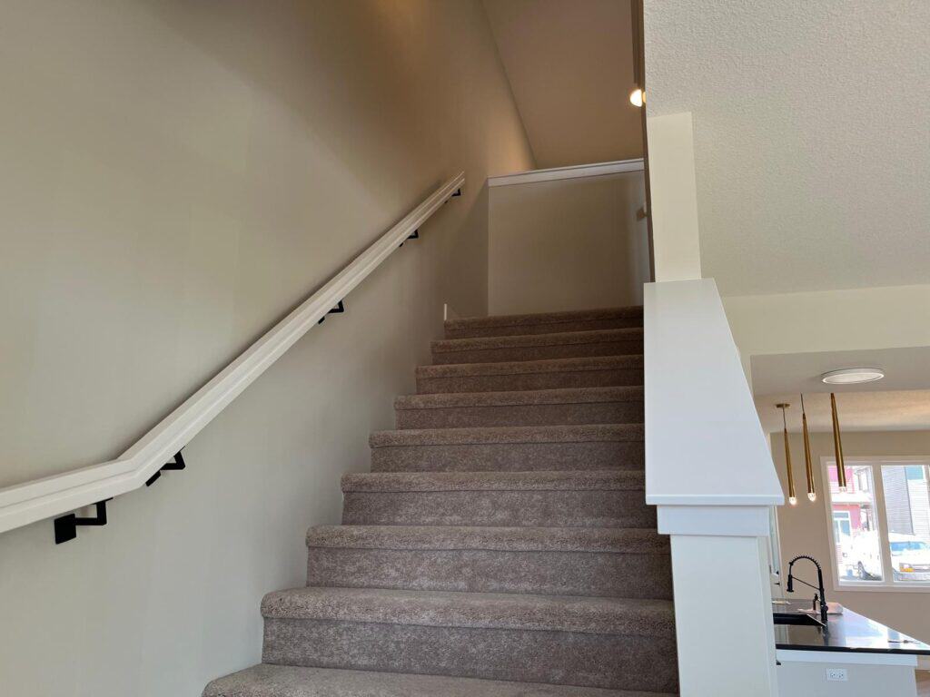 A professional interior staircase with beige carpet and white railing in a modern home, painted by Harding’s Painting in Calgary, Edmonton, Kelowna, H.