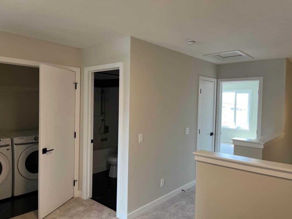 A residential laundry area with a washer and dryer, adjacent to a bathroom with a toilet, in a modern home interior with light-colored walls and natur.
